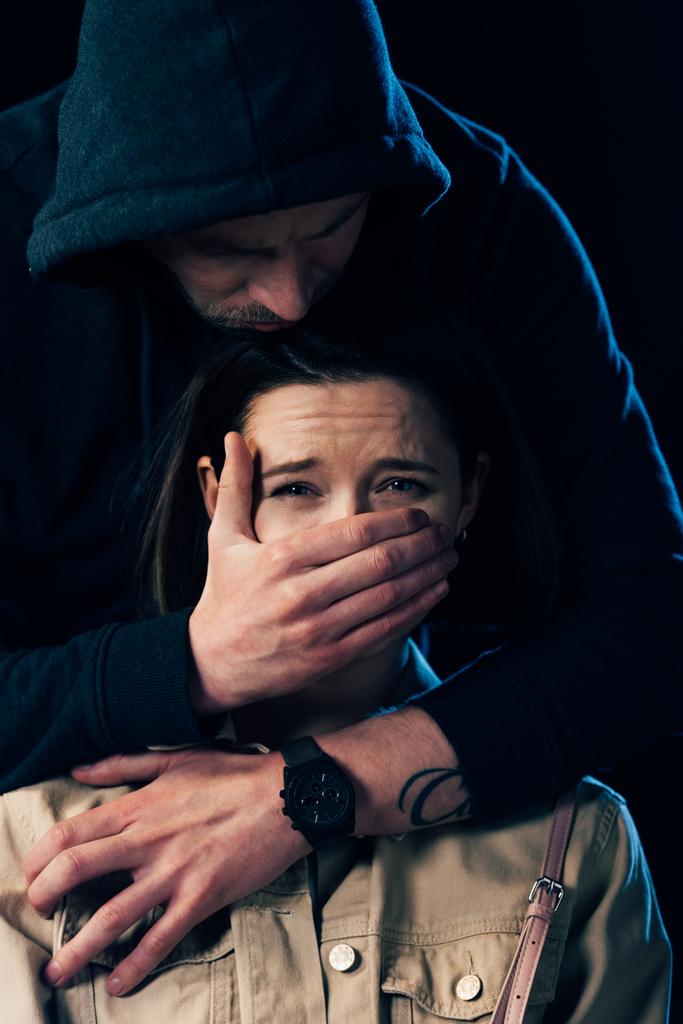 vista parcial de criminal atacando a mujer asustada y cubriéndose la boca aislada en negro
 - Foto, Imagen
