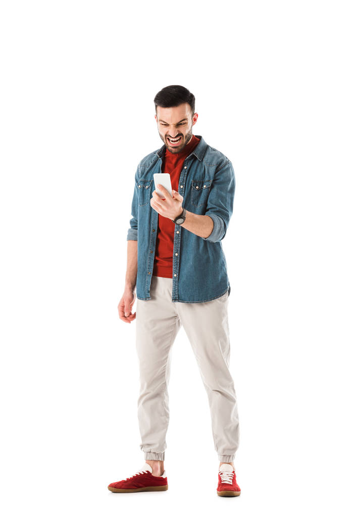 Irritierter Mann im Jeanshemd benutzt Smartphone isoliert auf weißem Grund - Foto, Bild