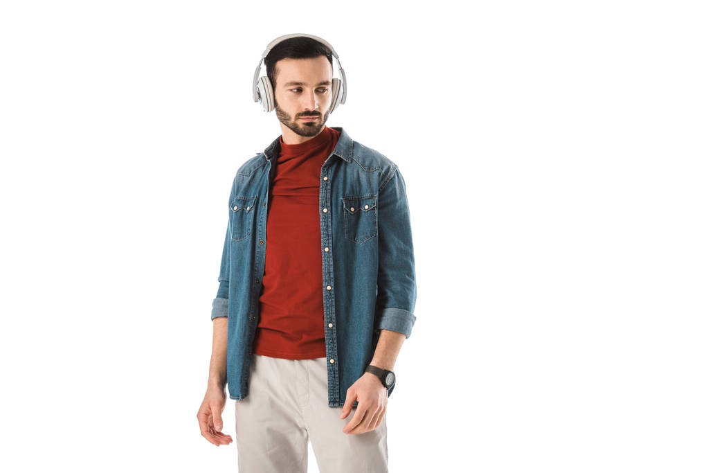 zasněný pohledný muž, který poslouchá hudbu ve sluchátkách izolovaných na bílém - Fotografie, Obrázek