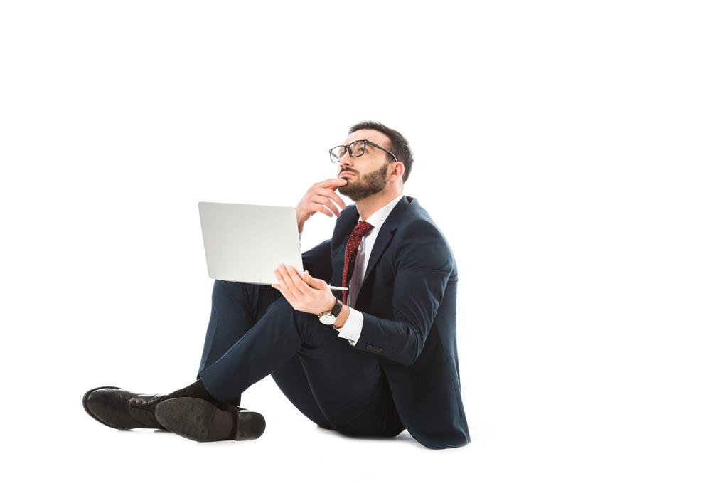 thoughtful businessman looking up while sitting with laptop on white background - Photo, Image