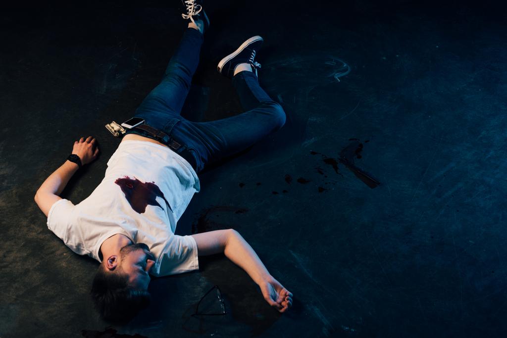 yleiskuva kuolleesta miehestä, jolla on verta t-paidassa, makaa rikospaikalla
 - Valokuva, kuva