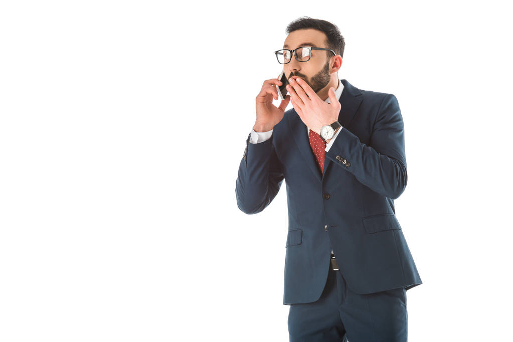шокированный бизнесмен закрывая рот рукой, разговаривая на смартфоне изолированы на белом
 - Фото, изображение