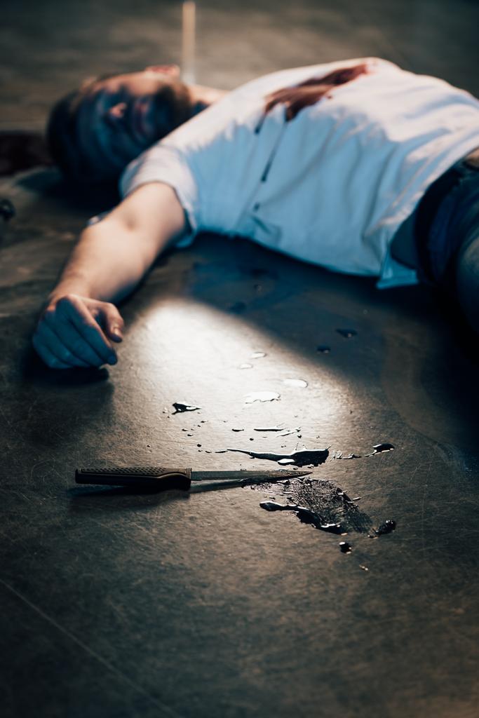 επιλεκτική εστίαση του νεκρού ανθρώπου με αίμα στο μπλουζάκι στο πάτωμα στον τόπο του εγκλήματος. - Φωτογραφία, εικόνα