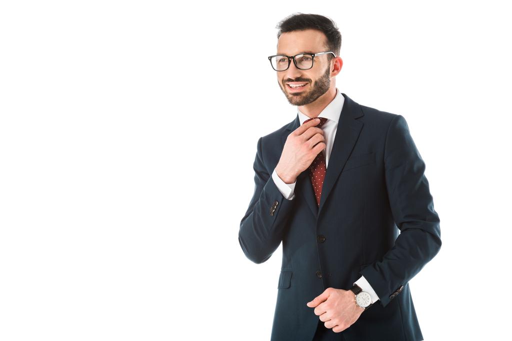 Красивый улыбающийся бизнесмен трогает галстук и смотрит в сторону изолированных на белом
 - Фото, изображение