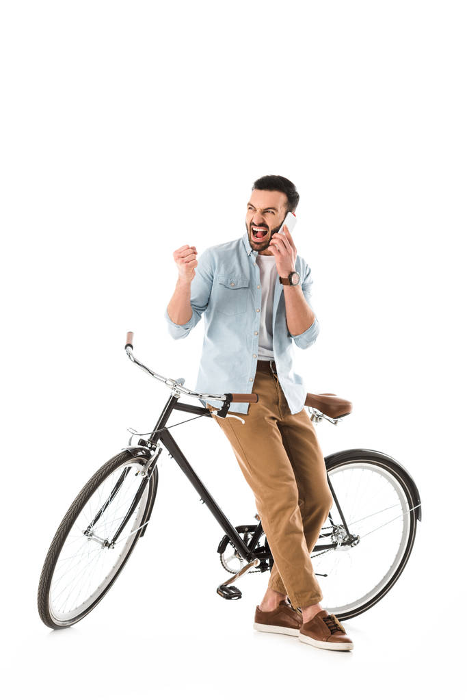 Wütender Mann mit Fahrrad streitet und zeigt Faust, während er auf Smartphone spricht - Foto, Bild