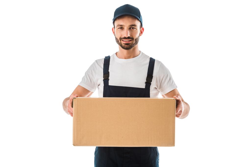 vrolijke knappe delivery man Holding kartonnen doos en glimlachend op camera geïsoleerd op wit - Foto, afbeelding