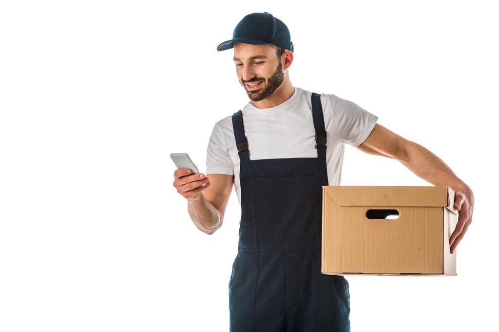 beyaz izole karton kutu tutarken akıllı telefon kullanarak neşeli yakışıklı teslimat adam - Fotoğraf, Görsel