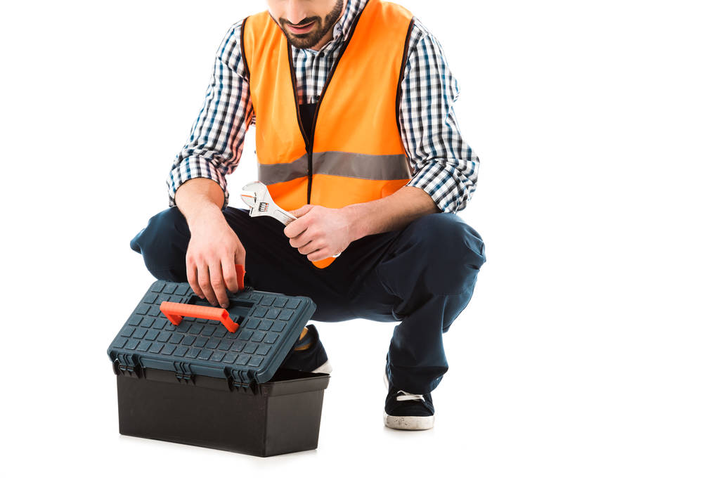 vista parcial del trabajador de la construcción consiguiendo llave ajustable de la caja de herramientas aislada en blanco
 - Foto, Imagen