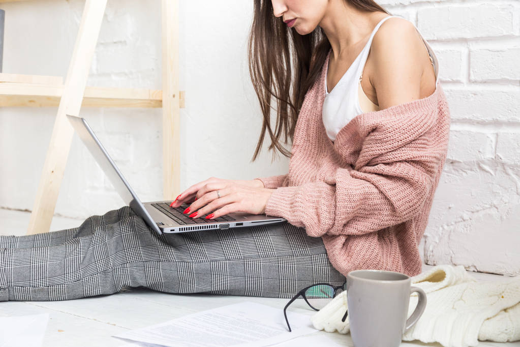 Fiatal nő ül a padlón egy skandináv lakás belsejében egy laptop, tanul jogot, szabadúszó lány a munkahelyen, távoktatási hallgató, online foglalkoztatás, papírmunka és kiszervezés koncepció - Fotó, kép