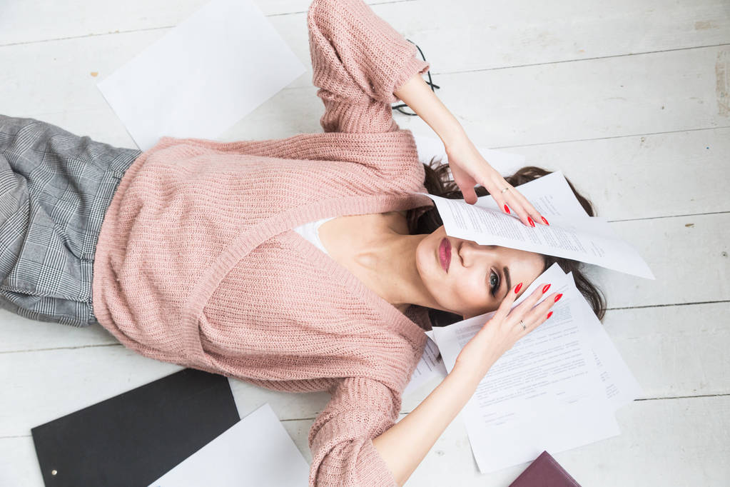Egy gyönyörű nő fekszik a padlón papírok és dokumentumok között, a lány szabadúszó mosolyog és lazít munka közben. - Fotó, kép