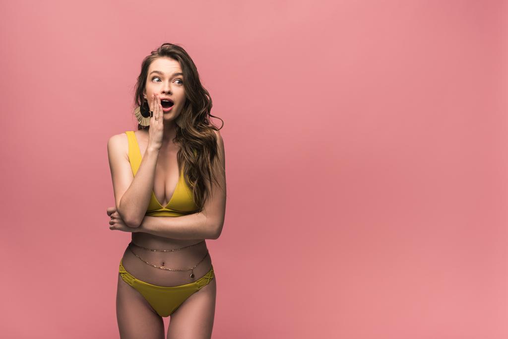 шокована молода жінка в жовтому купальнику дивиться ізольовано на рожевий
 - Фото, зображення