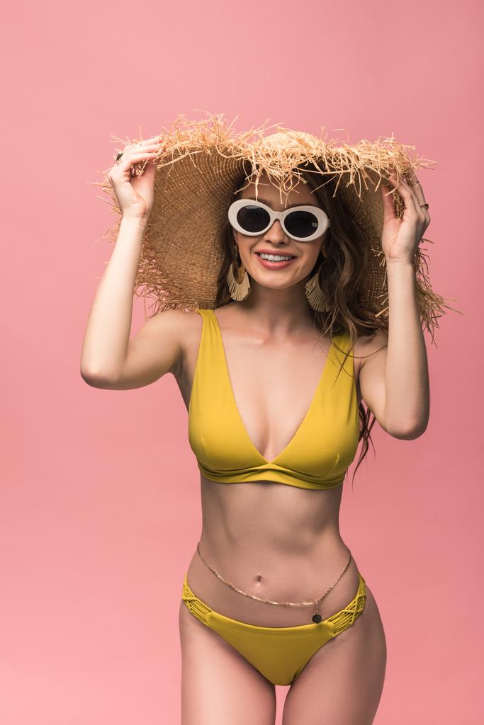 Очаровательная девушка в соломенной шляпе и солнечных очках улыбается изолированно на розовый
 - Фото, изображение
