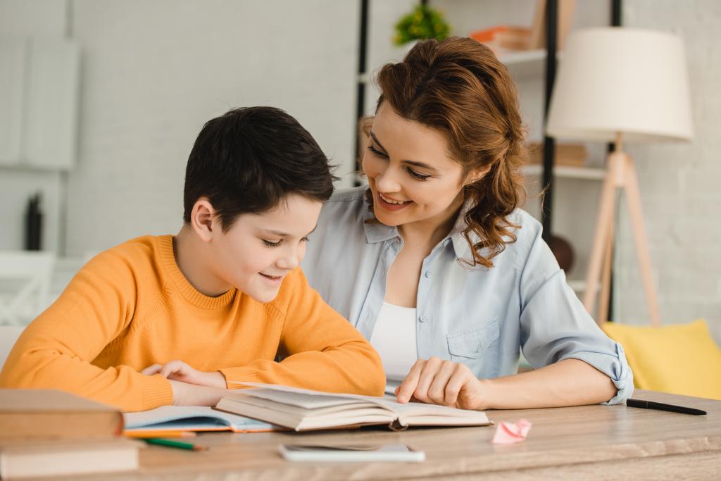 Lächelnde Mutter hilft entzückendem Sohn bei Hausaufgaben - Foto, Bild