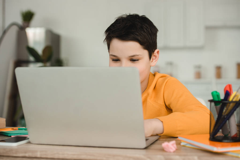 leuke school jongen met behulp van laptop terwijl het doen van school werk thuis - Foto, afbeelding