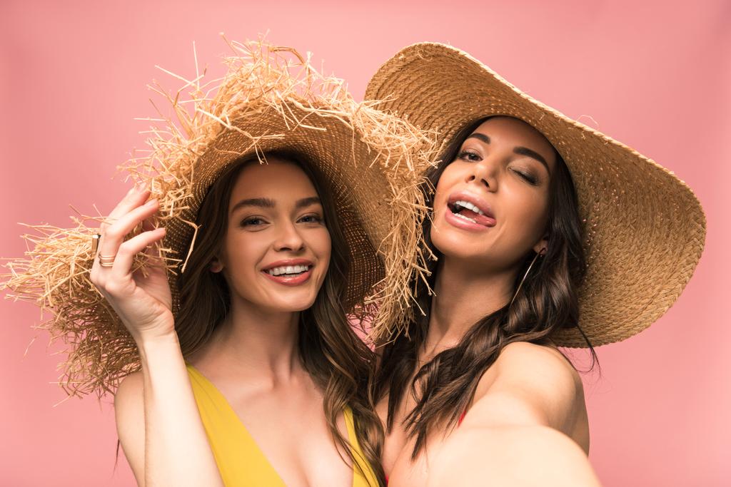 two smiling girls in straw hats taking selfie isolated on pink - Photo, Image