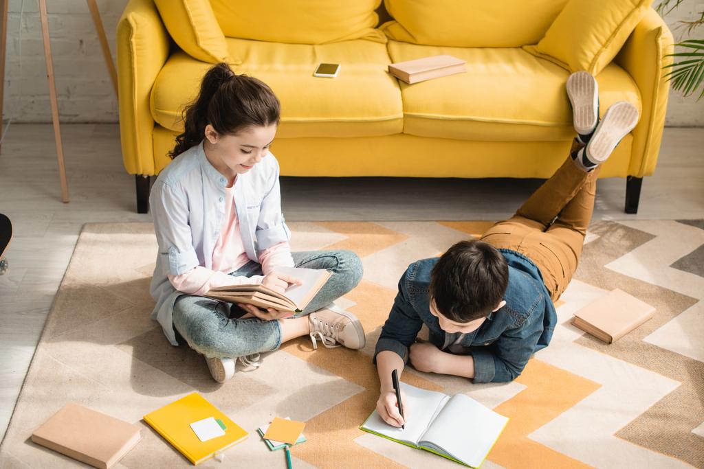 vista ad alto angolo di adorabili bambini che fanno i compiti sul pavimento a casa
 - Foto, immagini