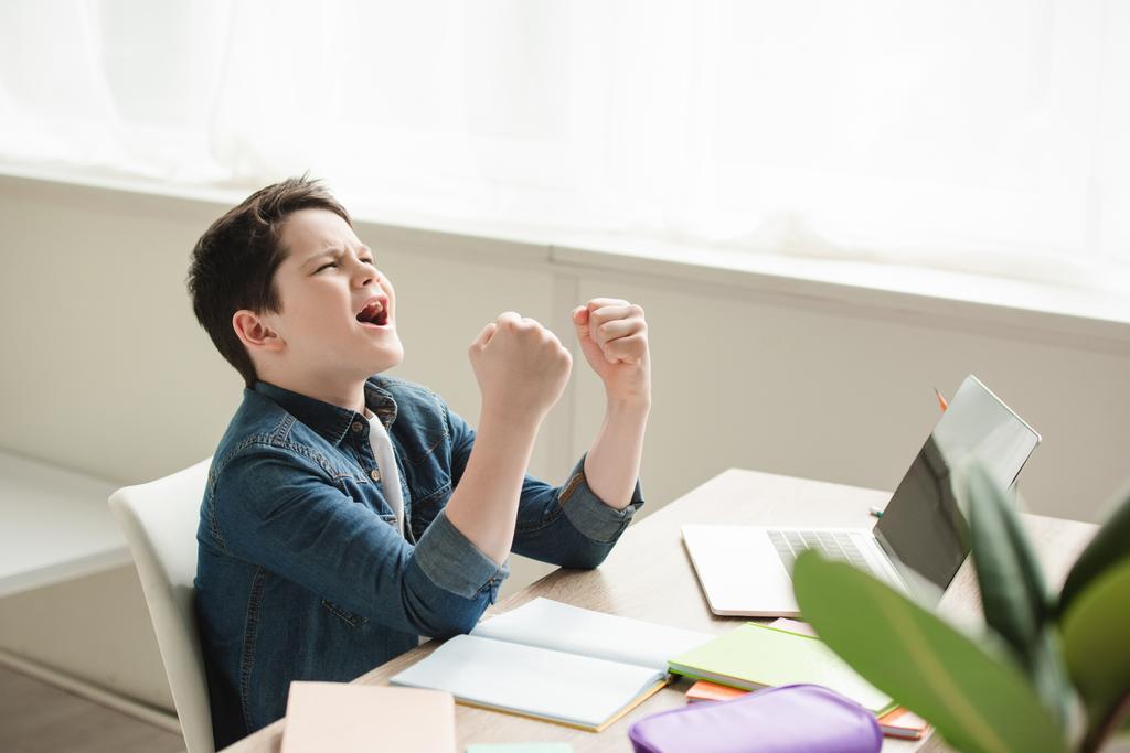 ενθουσιασμένος μαθητής δείχνει Ναι χειρονομία, ενώ κάθονται στο γραφείο και να κάνει την εργασία - Φωτογραφία, εικόνα