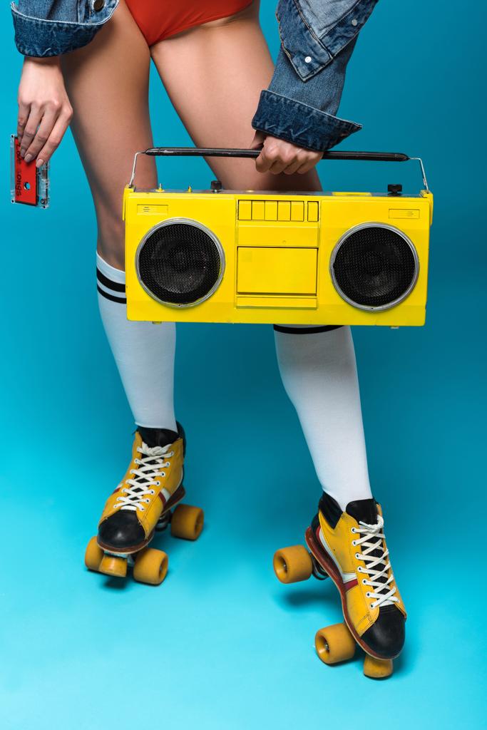 cropped view of woman in swimsuit and roller skates holding boombox and cassette tape on blue - Photo, Image