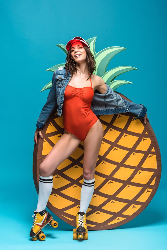 full length view of woman in swimsuit and roller skates standing near decorative pineapple on blue - Photo, Image