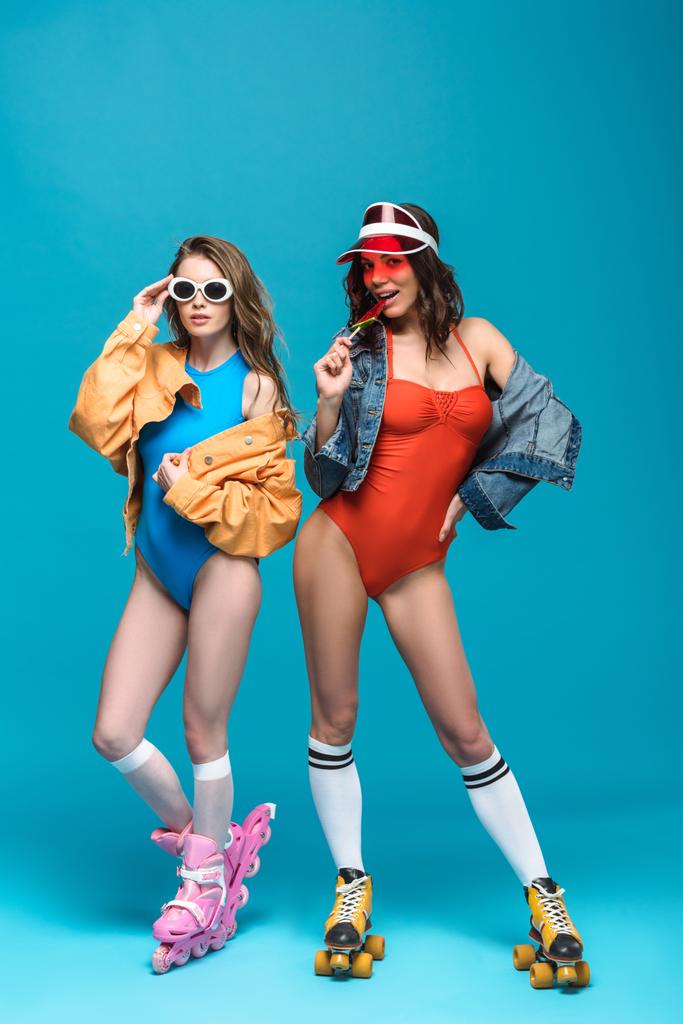 full length view of two stylish girls in roller skates with watermelon lollipop on blue - Photo, Image
