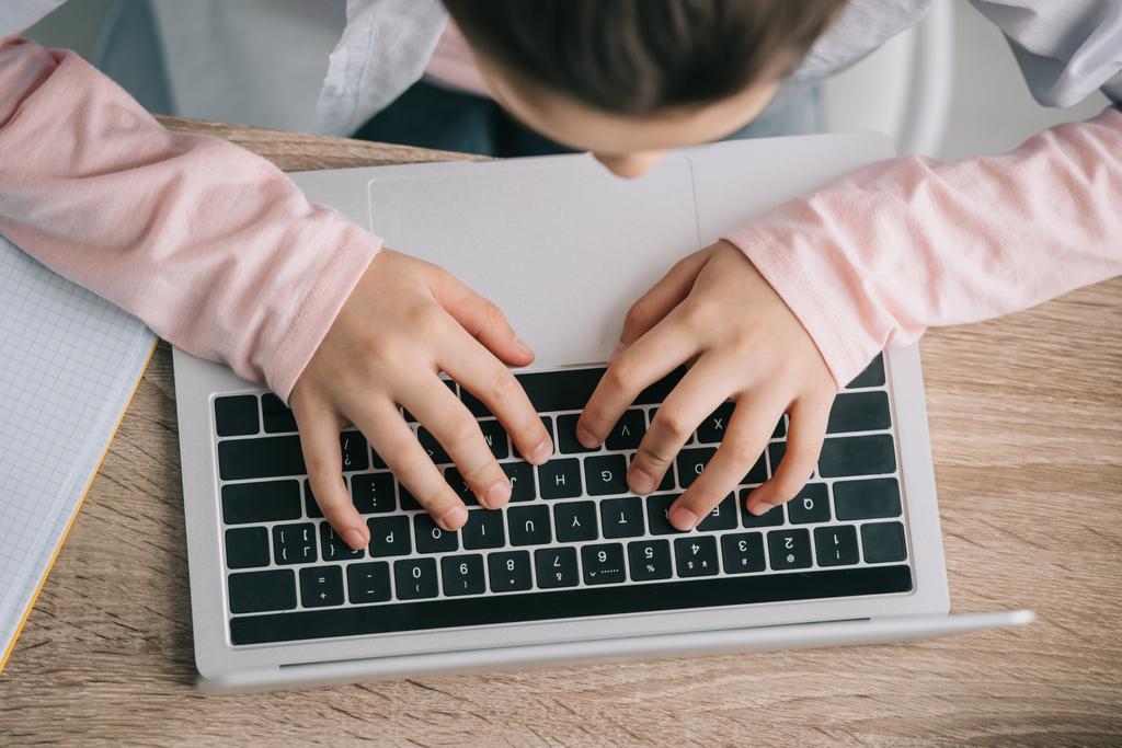 bijgesneden beeld van school kind met laptop terwijl zittend op Bureau en het doen van huiswerk - Foto, afbeelding