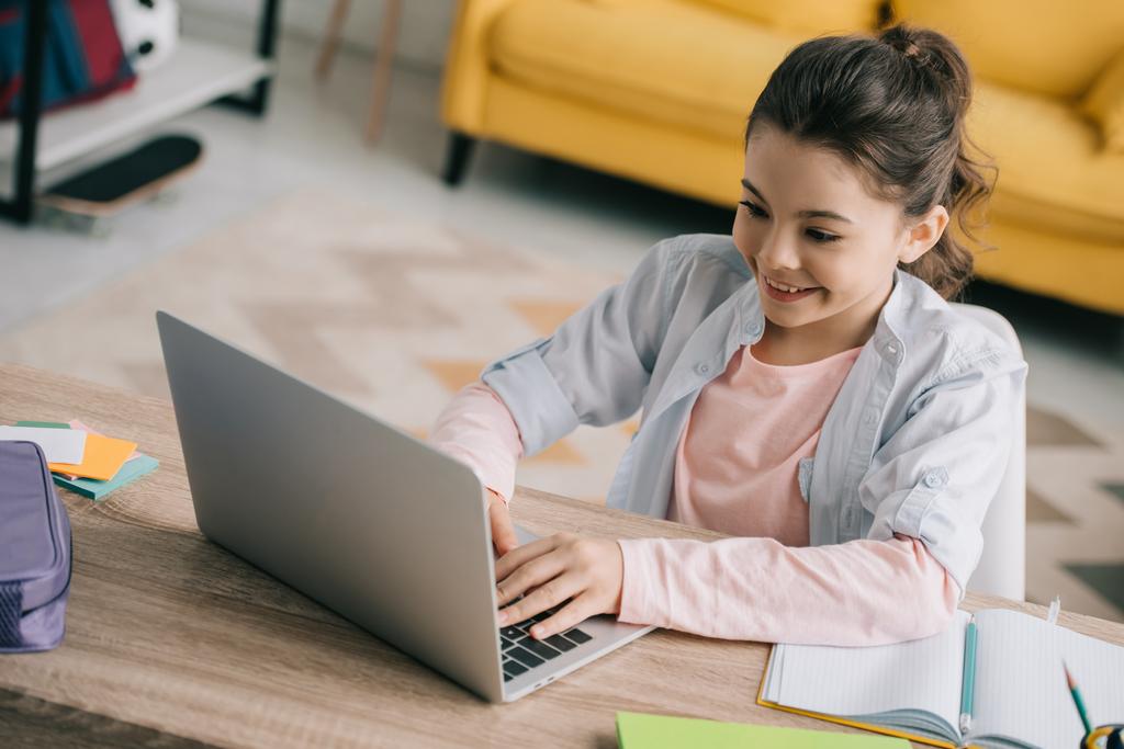 Widok z wysokim kątem uśmiechnięty uczeń przy użyciu laptopa, siedząc przy drewnianym biurku w domu - Zdjęcie, obraz
