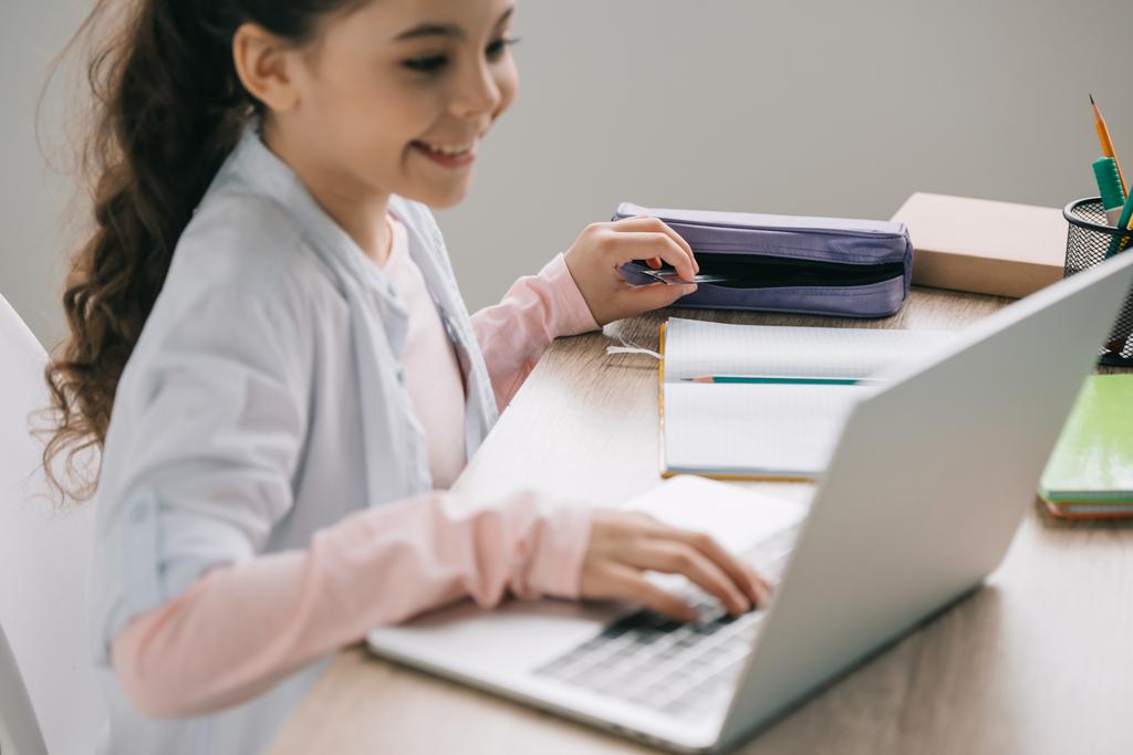 вибірковий фокус усміхненої школярки, що витягує лінійку з пенала під час використання ноутбука вдома
 - Фото, зображення