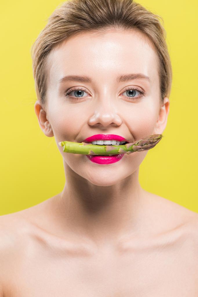 fröhliche nackte Frau mit grünem und schmackhaftem Spargel im Mund, isoliert auf gelb  - Foto, Bild