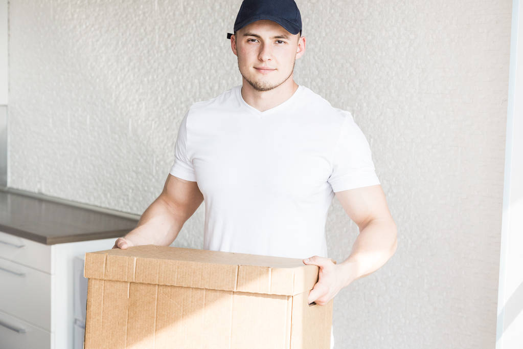Доставка сильного, мускулистого человека, загружающего картонные коробки для переезда в квартиру. профессиональный транспортник, мужчина-погрузчик в комбинезоне. Свободное место для текста, изолированные
 - Фото, изображение