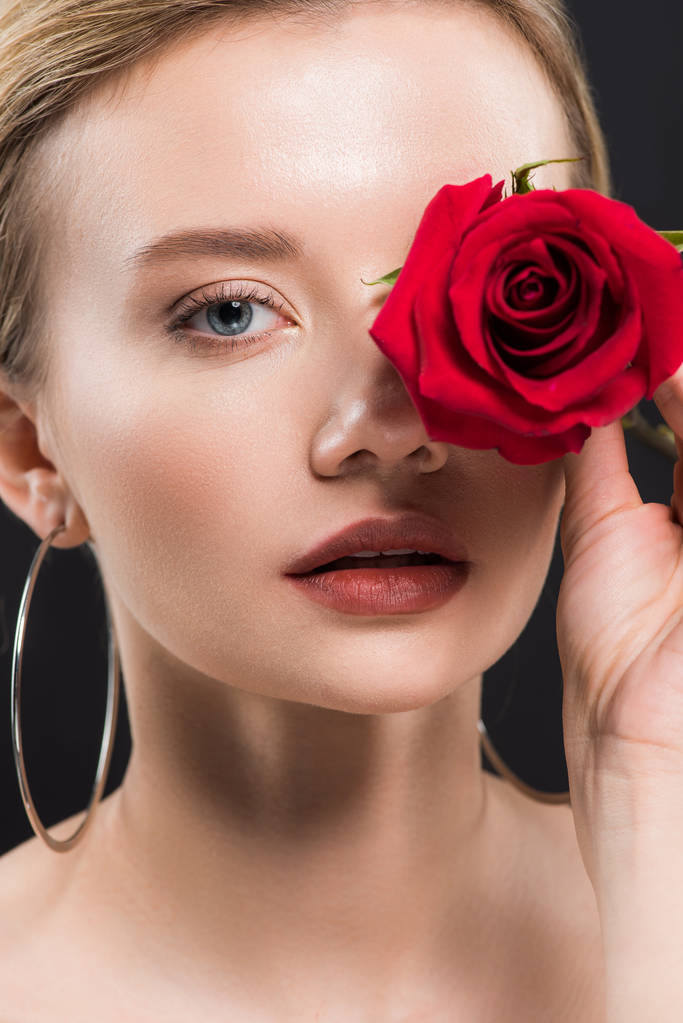 selective focus of attractive young woman holding red rose isolated on black  - Photo, Image