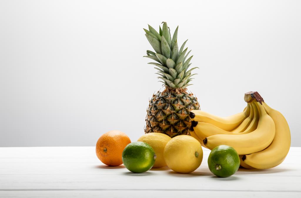 zralé banány v blízkosti sladkého ananasu, citronů, pomerančů a vápna na bílém  - Fotografie, Obrázek