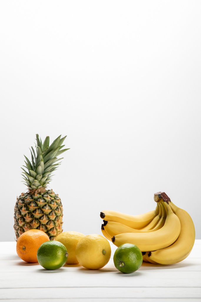 gele bananen bij zoete ananas, citroenen, sinaasappel en limoenen op wit  - Foto, afbeelding