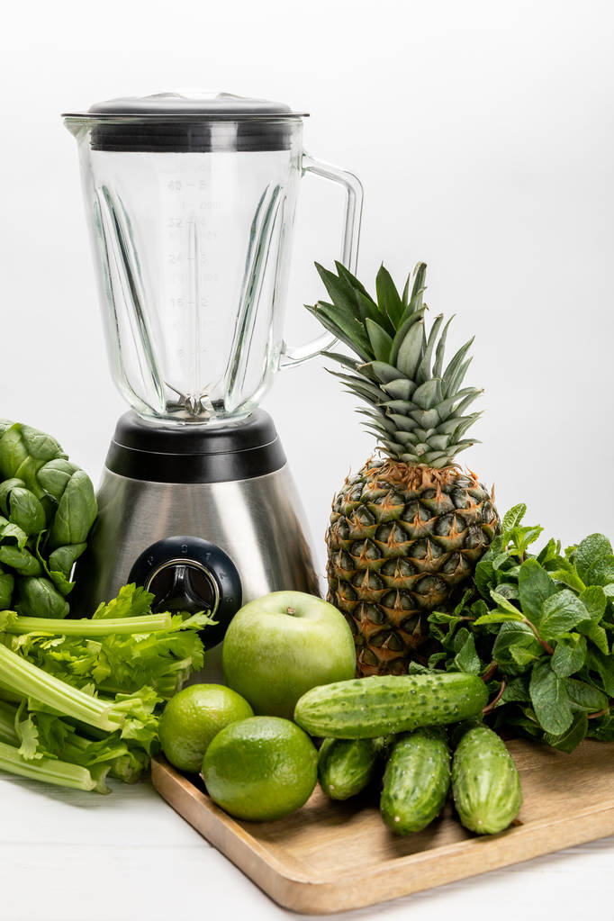 blender near green fresh spinach leaves, organic celery, cucumbers and fruits on white  - Photo, Image