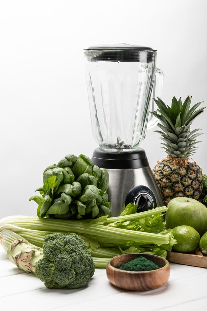 το μπλέντερ κοντά σε φρέσκα, πράσινα λαχανικά και βιολογικά φρούτα σε λευκό  - Φωτογραφία, εικόνα