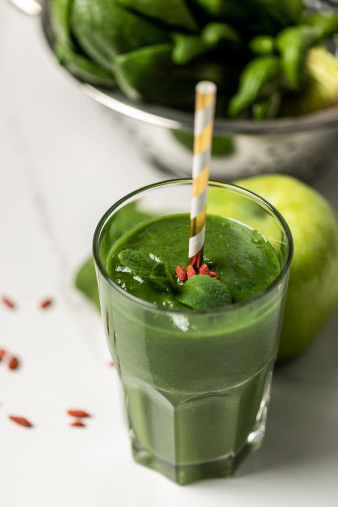 selectieve focus van smakelijke smoothie in glas met stro in de buurt van spinazie bladeren en appel op wit  - Foto, afbeelding