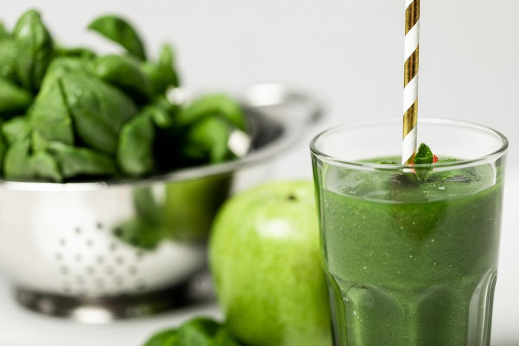 foco seletivo de smoothie verde saboroso em vidro com palha perto de folhas de espinafre e maçã em branco
  - Foto, Imagem