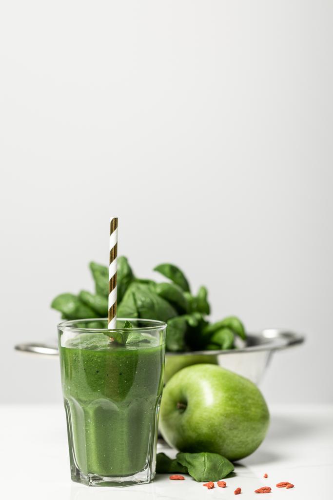 szelektív középpontjában a zöld smoothie üveg szalma közelében friss spenót levelek és alma a szürke  - Fotó, kép