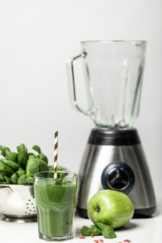 foyer sélectif de smoothie vert en verre avec de la paille près des feuilles d'épinards, pomme et mélangeur sur blanc
  - Photo, image