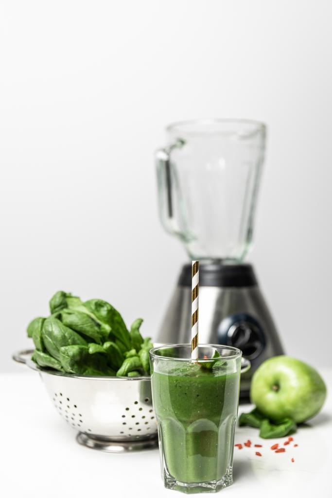 szelektív középpontjában a zöld smoothie üveg szalma közelében friss spenót levelek, ízletes alma és turmixgép fehér  - Fotó, kép