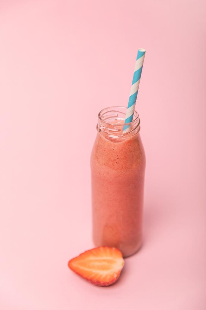 γλυκό και νόστιμο ρόφημα σε γυάλινο μπουκάλι με άχυρο κοντά σε ώριμες φράουλες απομονωμένες σε ροζ  - Φωτογραφία, εικόνα