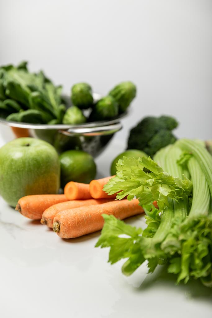 selectieve focus van selderij bij wortelen, rijpe appel en groene groenten op grijs  - Foto, afbeelding