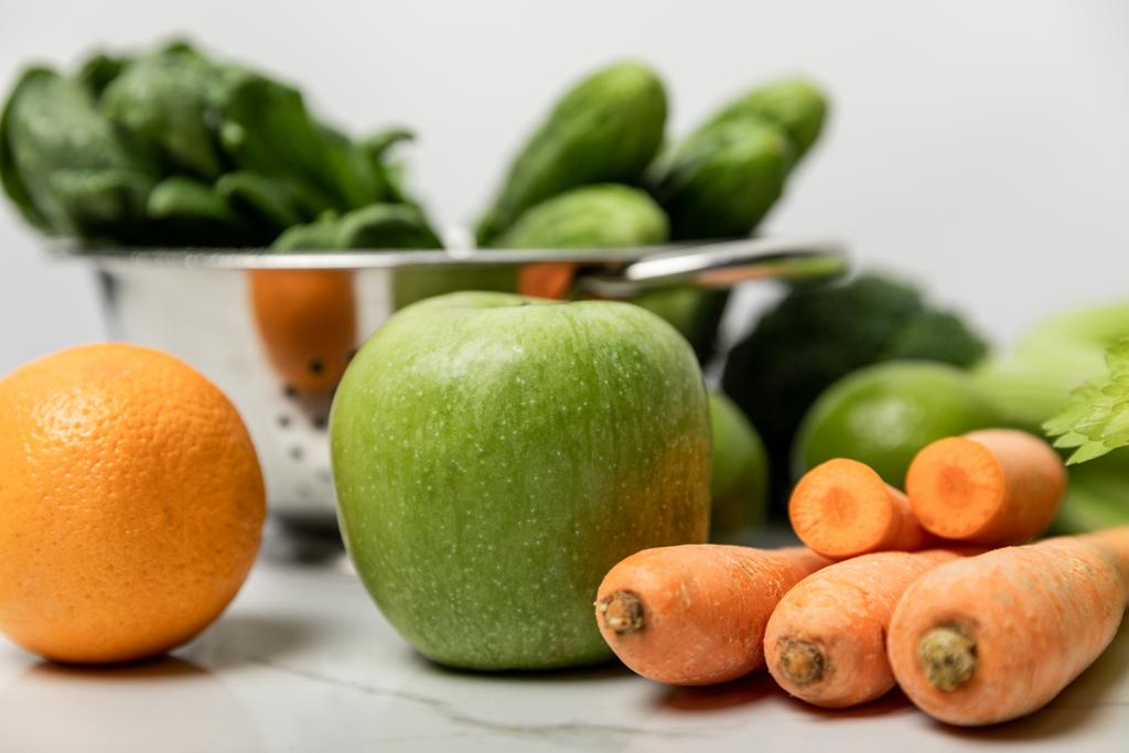 selective focus of green apple, orange and carrots near green cucumbers on white  - Photo, Image