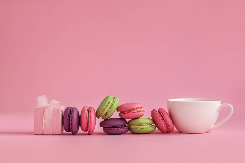 Розовый подарок и рожь французских цветных макарон и чашка кофе, лежащие на розовом фоне
 - Фото, изображение