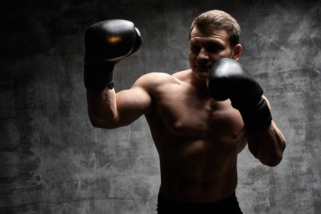 Μυϊκή αντλούσα άντρα πυγμαχία σε γάντια σε μαύρο φόντο. Σέξι αθλητικό σώμα - Φωτογραφία, εικόνα