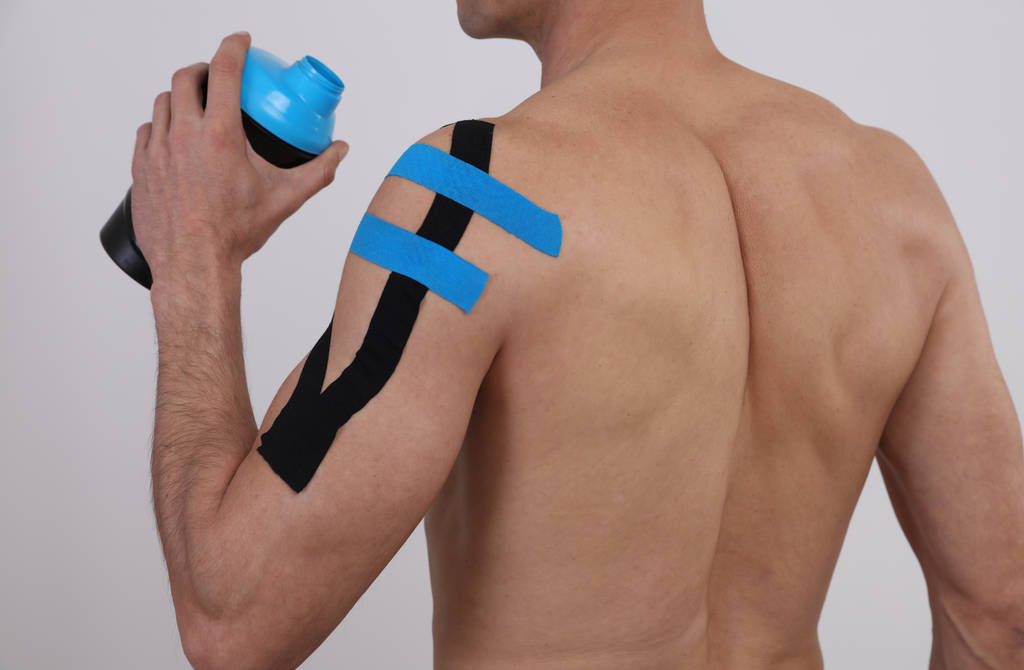 Kinesiologie se tapisuje. Sportovní muž, který uplatňuje poranění, bolest na rameni. Koncepce alternativních léků - Fotografie, Obrázek