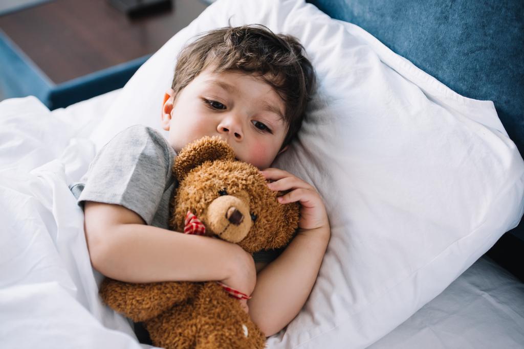 мила дитина лежить в ліжку з плюшевим ведмедем вдома
  - Фото, зображення