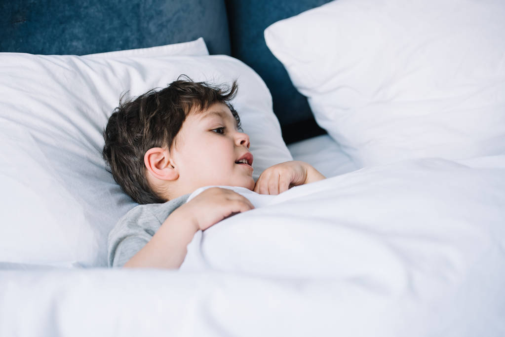 χαριτωμένο παιδί ξαπλωμένο σε λευκό μαξιλάρι στο κρεβάτι στο σπίτι  - Φωτογραφία, εικόνα