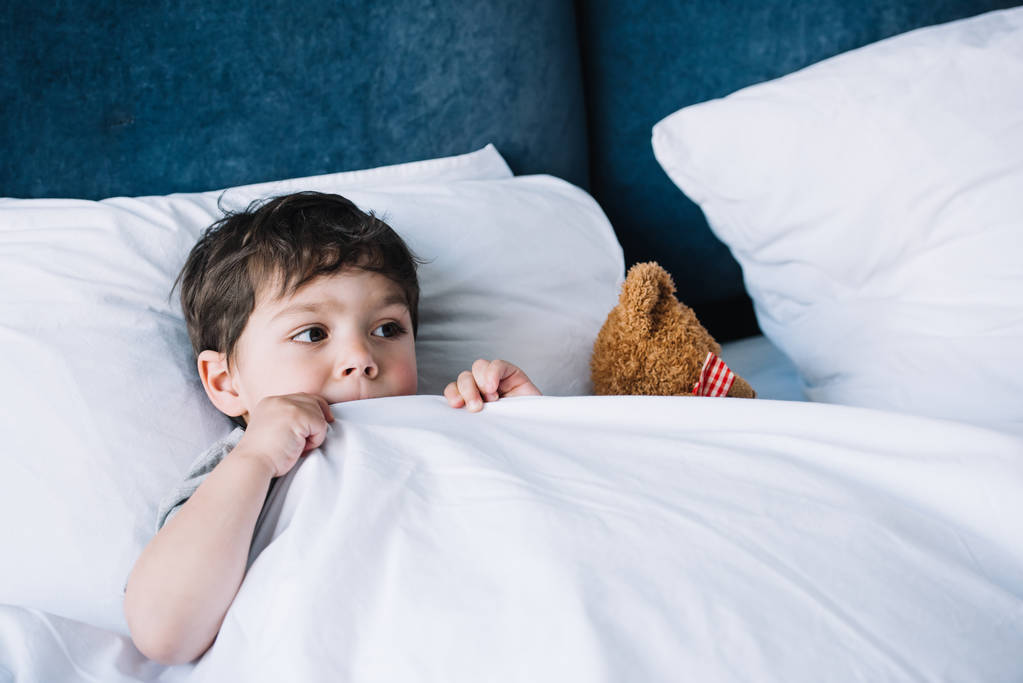 Kind liegt auf weißem Kissen im Bett neben Teddybär zu Hause - Foto, Bild