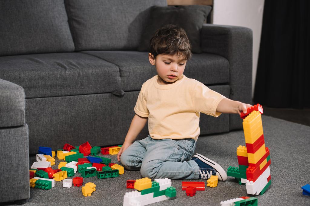 entzückendes Kleinkind spielt mit bunten Spielzeugklötzen, während es im Wohnzimmer auf dem Boden sitzt  - Foto, Bild