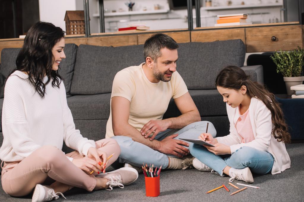 щасливі батьки сидять на підлозі біля милої дочки малюють на папері
  - Фото, зображення